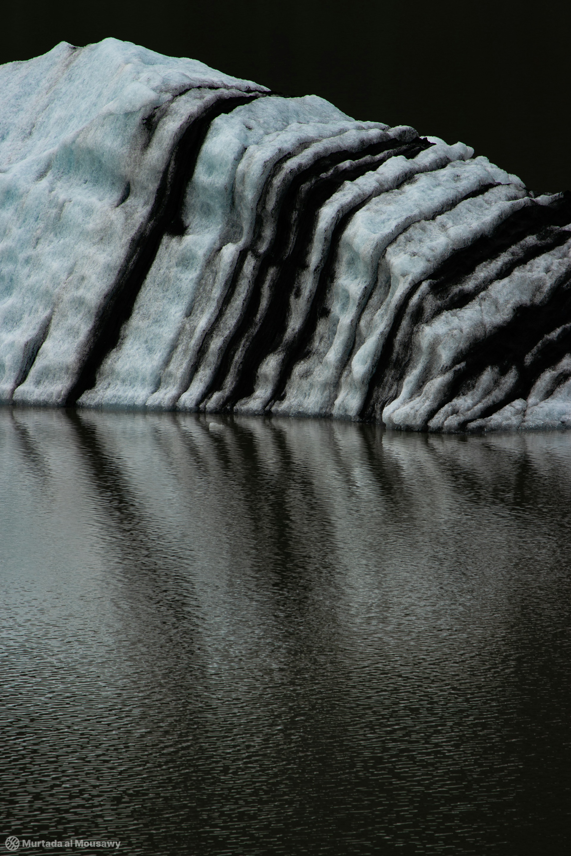 Photo of glacial ice of Iceland, reflected in a river with black and cyan blue stripes