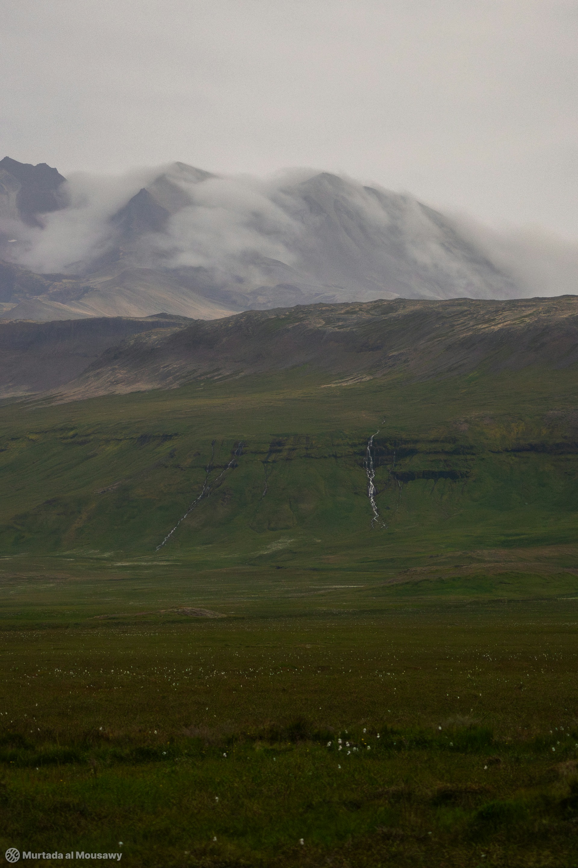 Photo of a distant landscape of fog covered green mountains in Iceland.