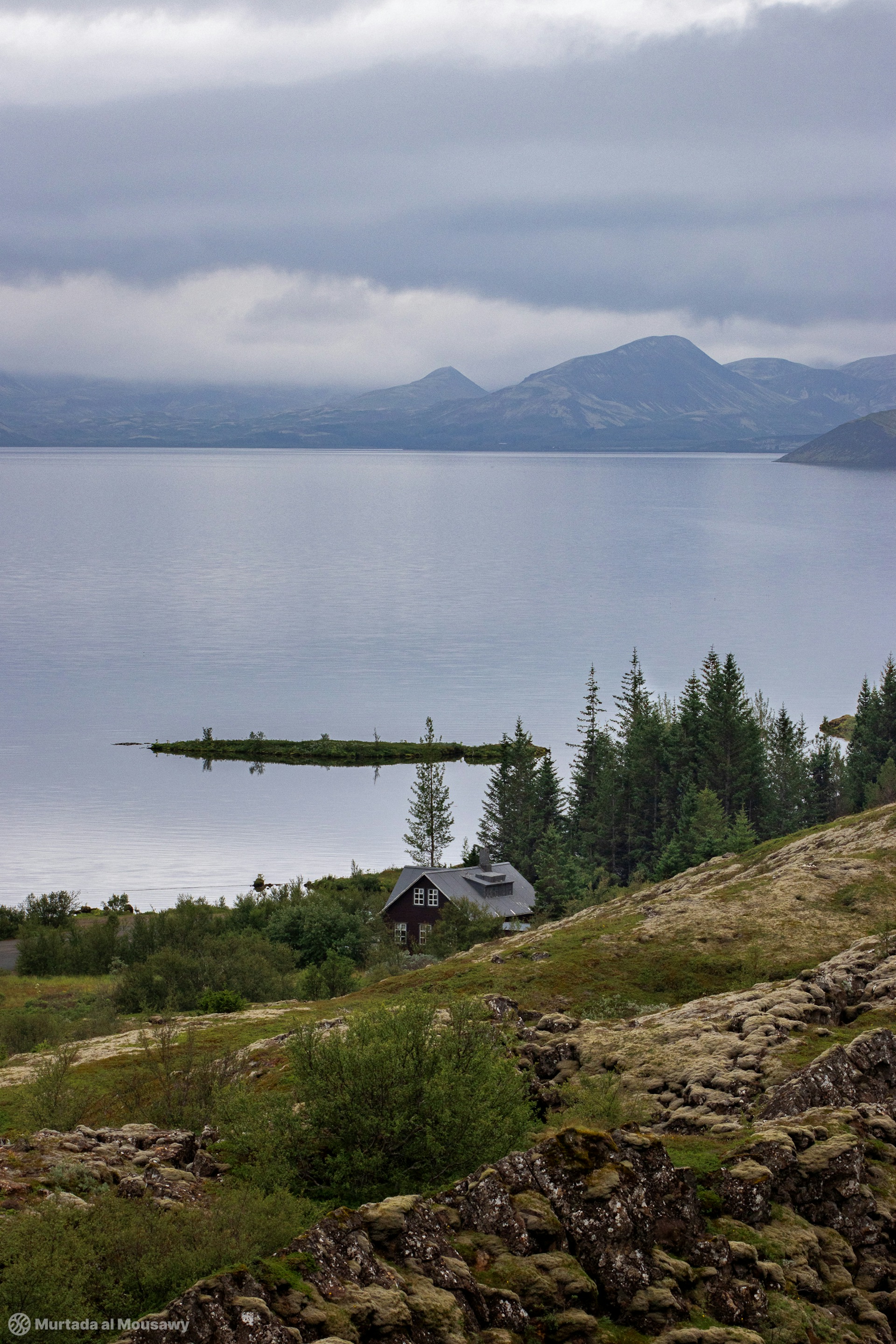 Landscape photo of a big lake and a cabin on a hill in Iceland.