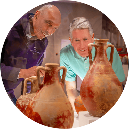 Two men view two ancient clay vases in a museum case.