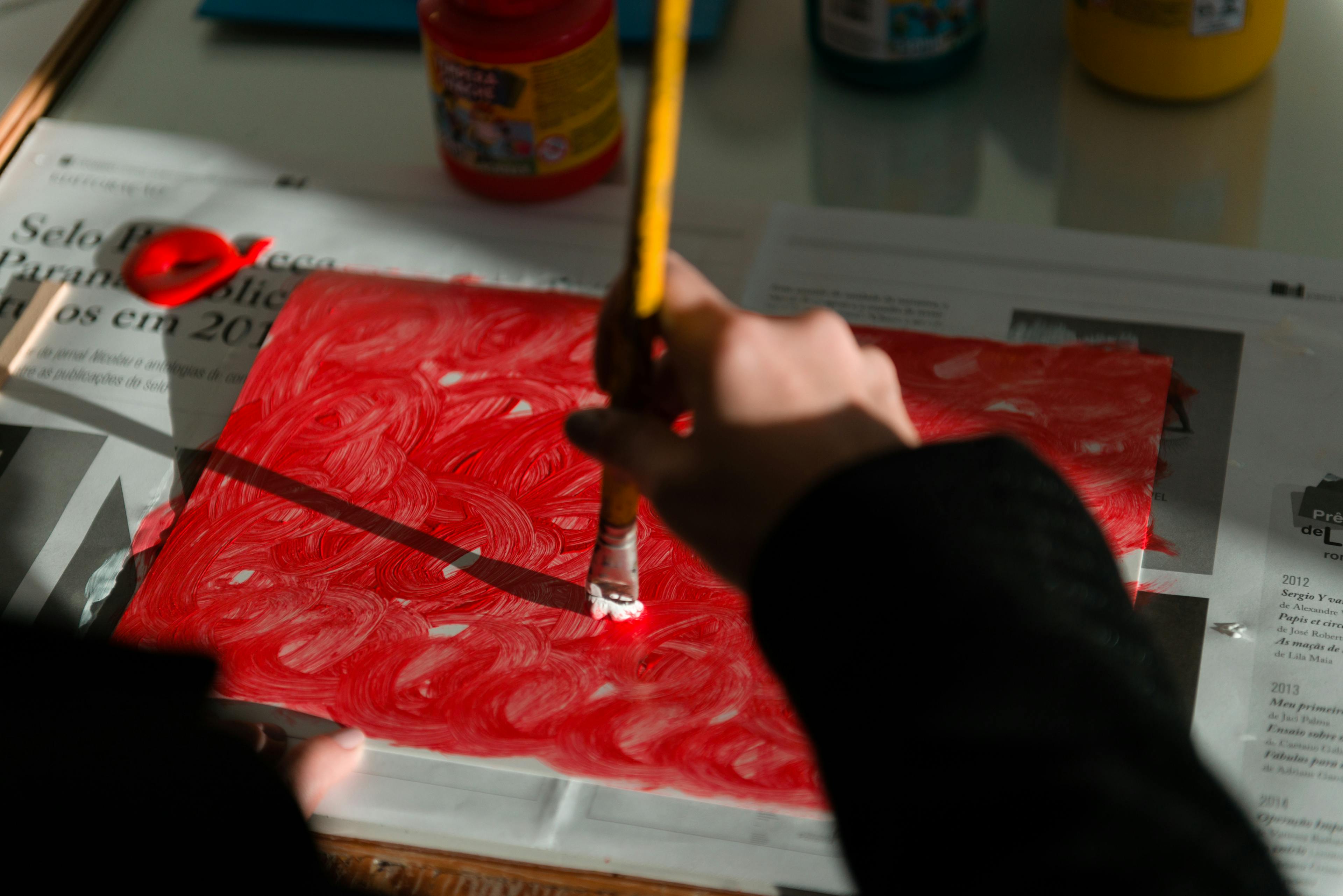 Mão pintando de vermelho uma folha de papel
