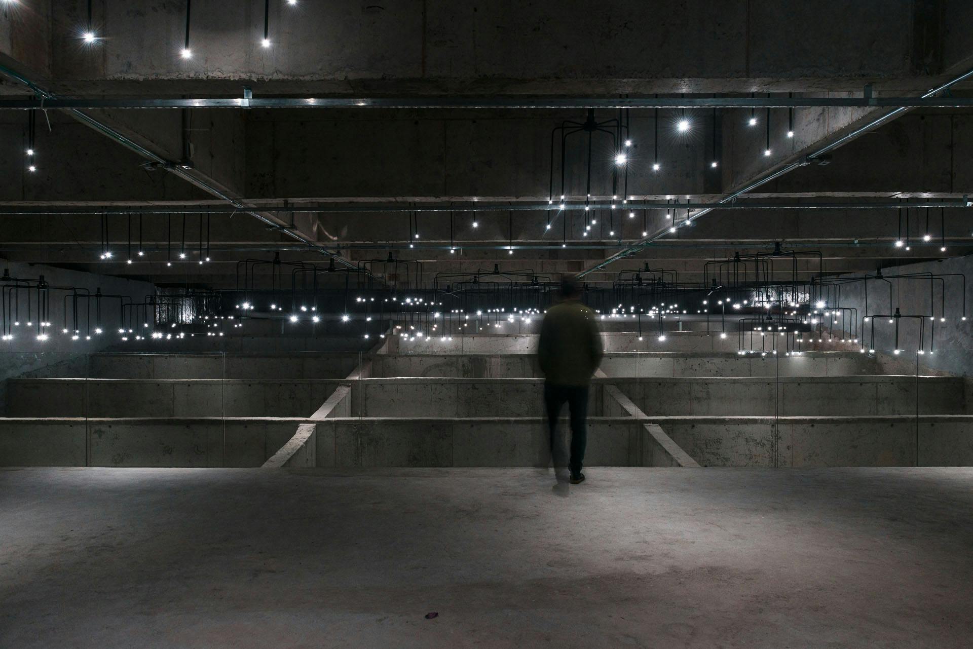 Sala expositiva da mostra Luz e Espaço. Vulto observa luzes piscarem no concreto.