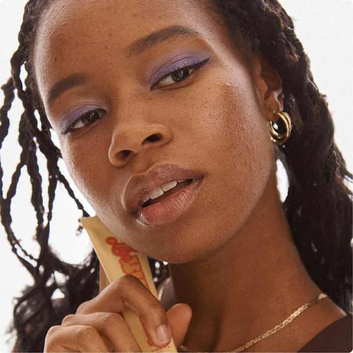 A young Black woman looking just beyond the camera with the Topicals "Like Butter" product in her hands