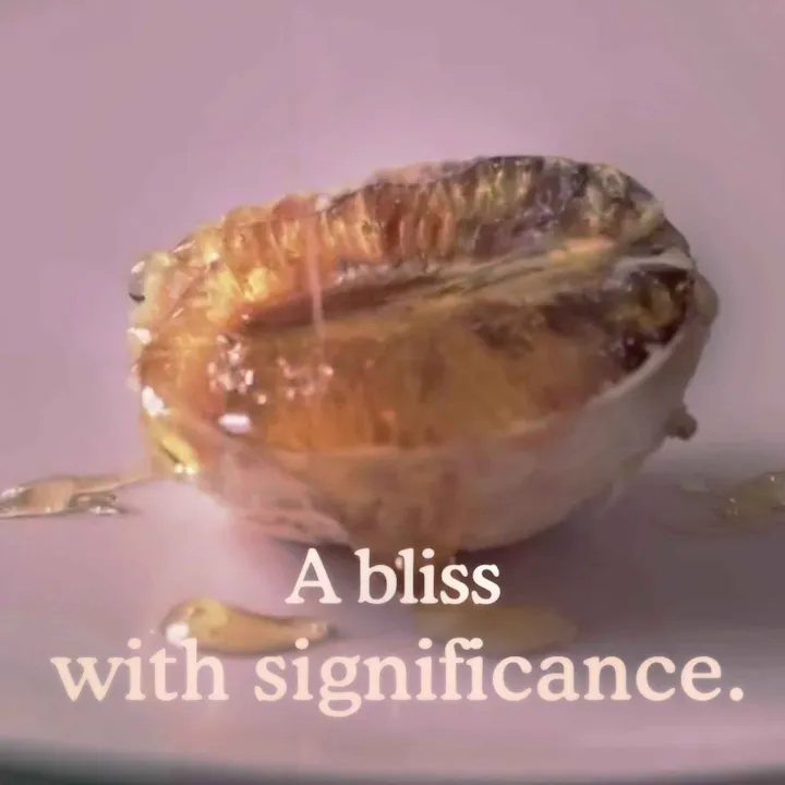 A blood orange on a pink background with honey dripped all over it, with text on top that says "A bliss with significance"