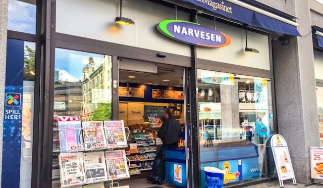 A Narvesen convenience store in Norway with newspaper displays at the entrance and a person visible inside the shop.