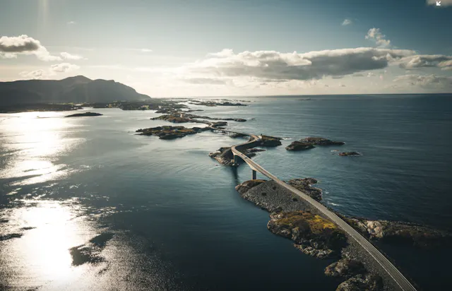 Aerial photo of a coastal road bridge winding over small islands and skerries in the sea with mountains in the distance.