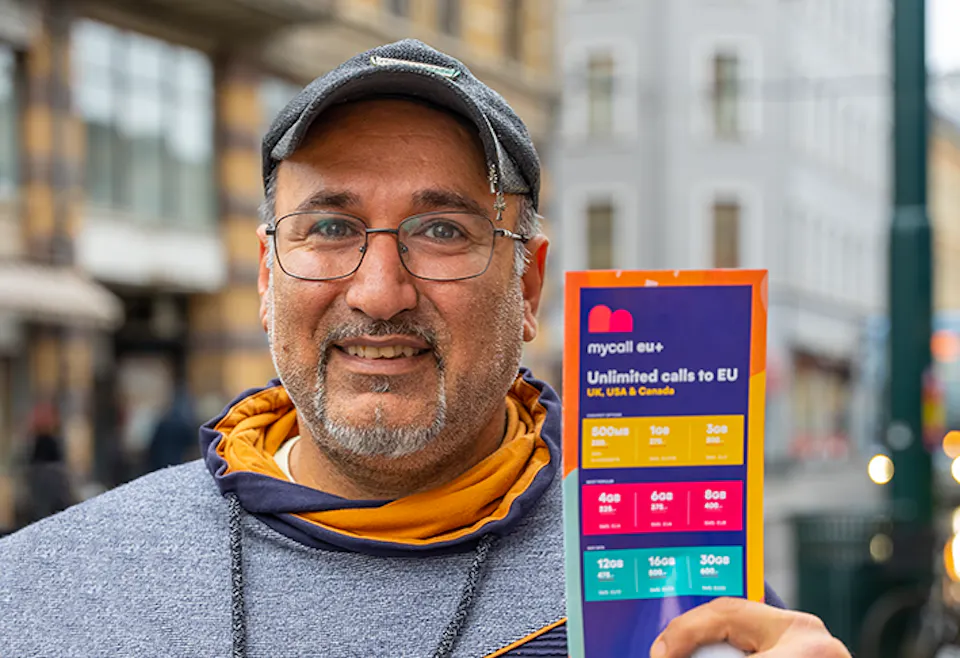 Man in grey sweater holding a colourful Mycall EU+ brochure showing unlimited calls to EU.