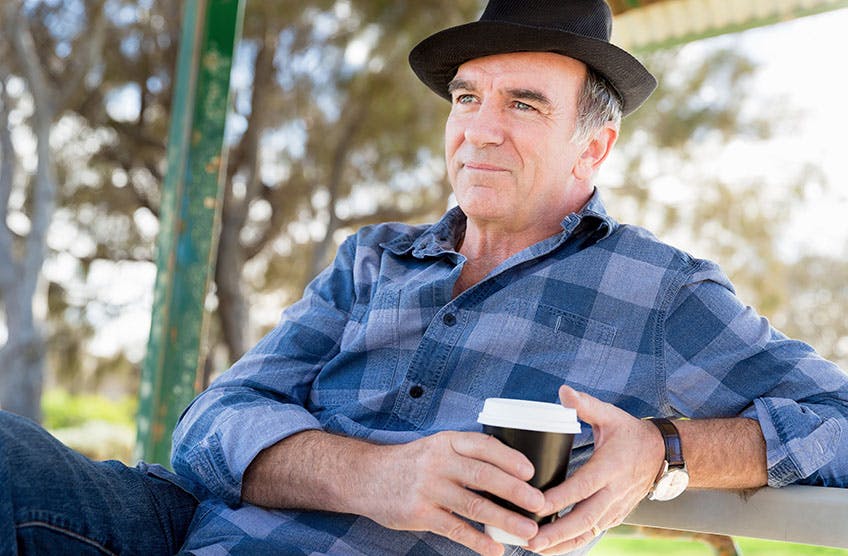 Older man sitting on bench with coffee