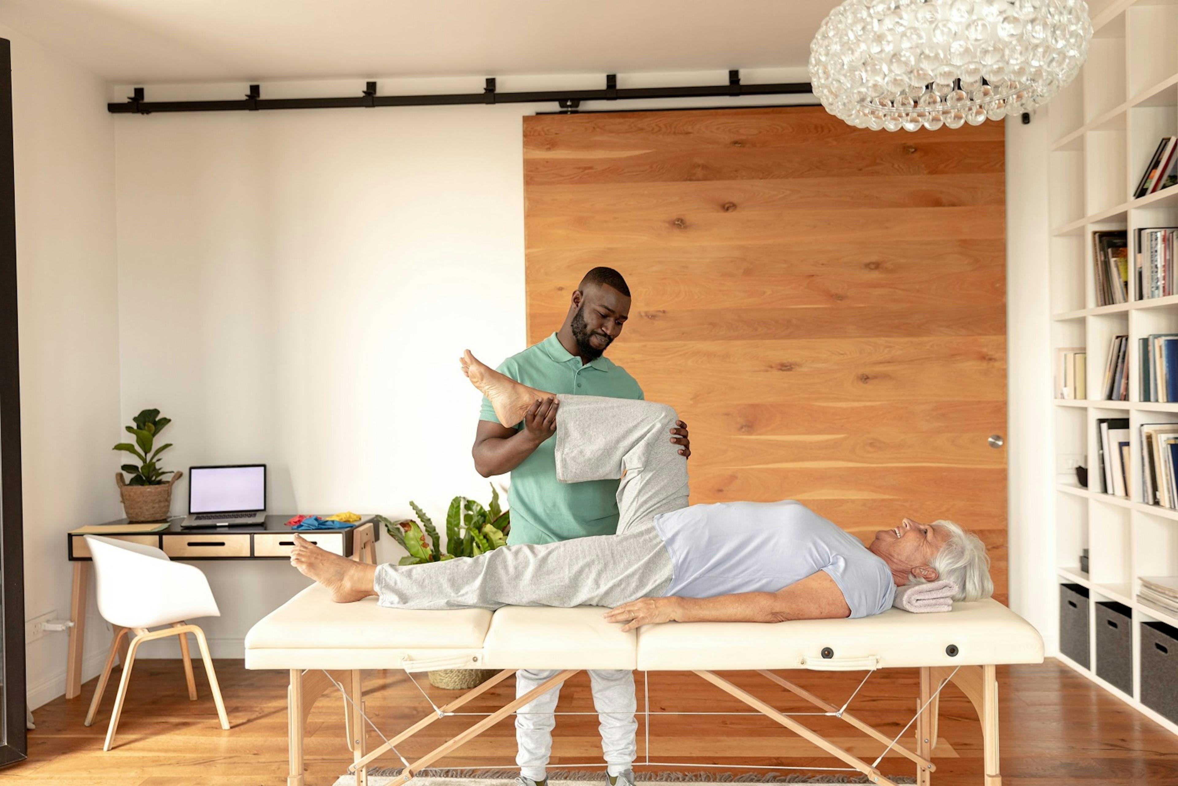 An occupational therapist massages a patient's legs in her home