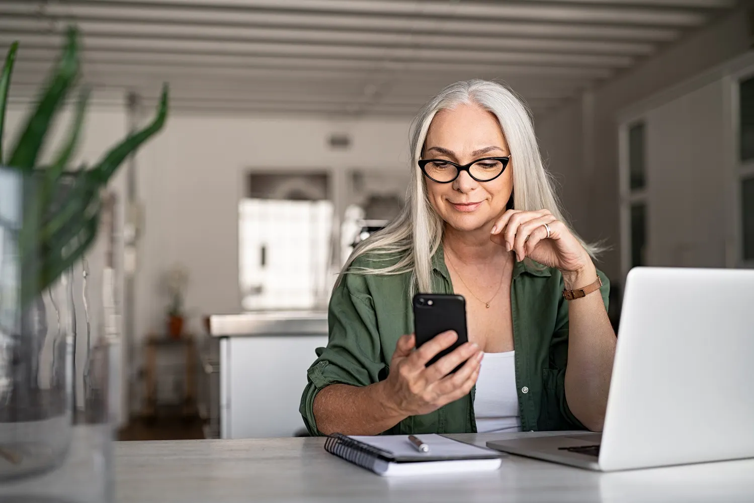 Woman on laptop looking at her phone