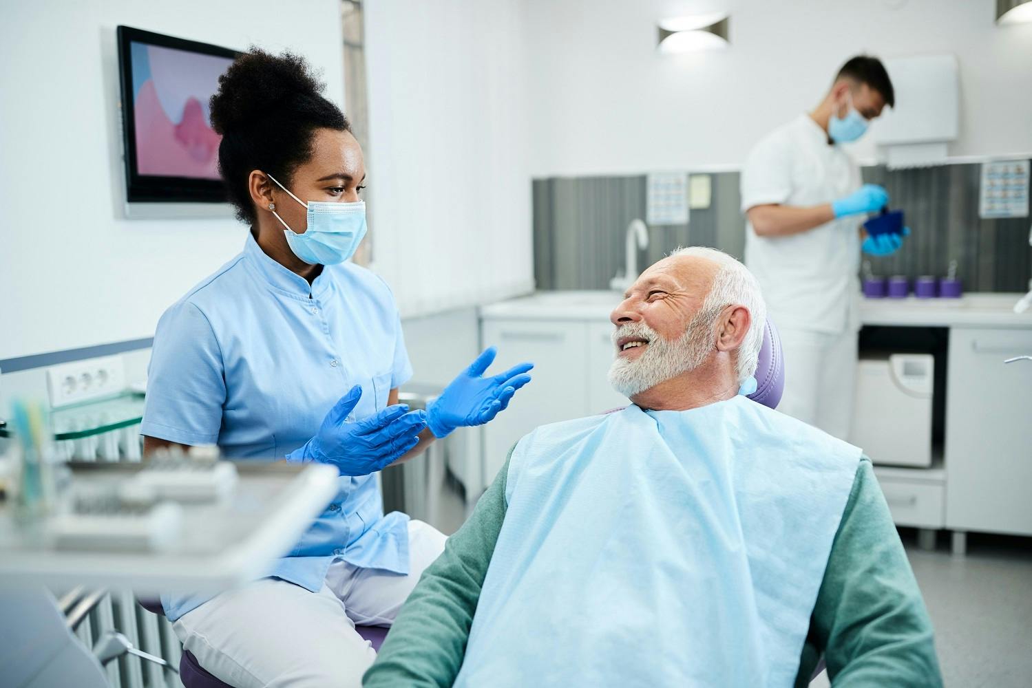 A male patient in a dental chair with a female dentist explaining a procedure