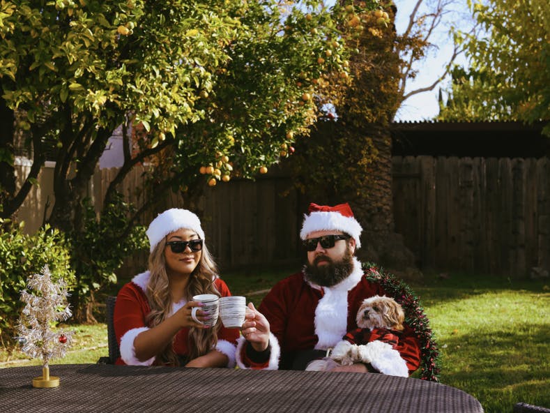 Un couple et leur chien déguisés avec des déguisements de Noël, buvant un café dans leur jardin