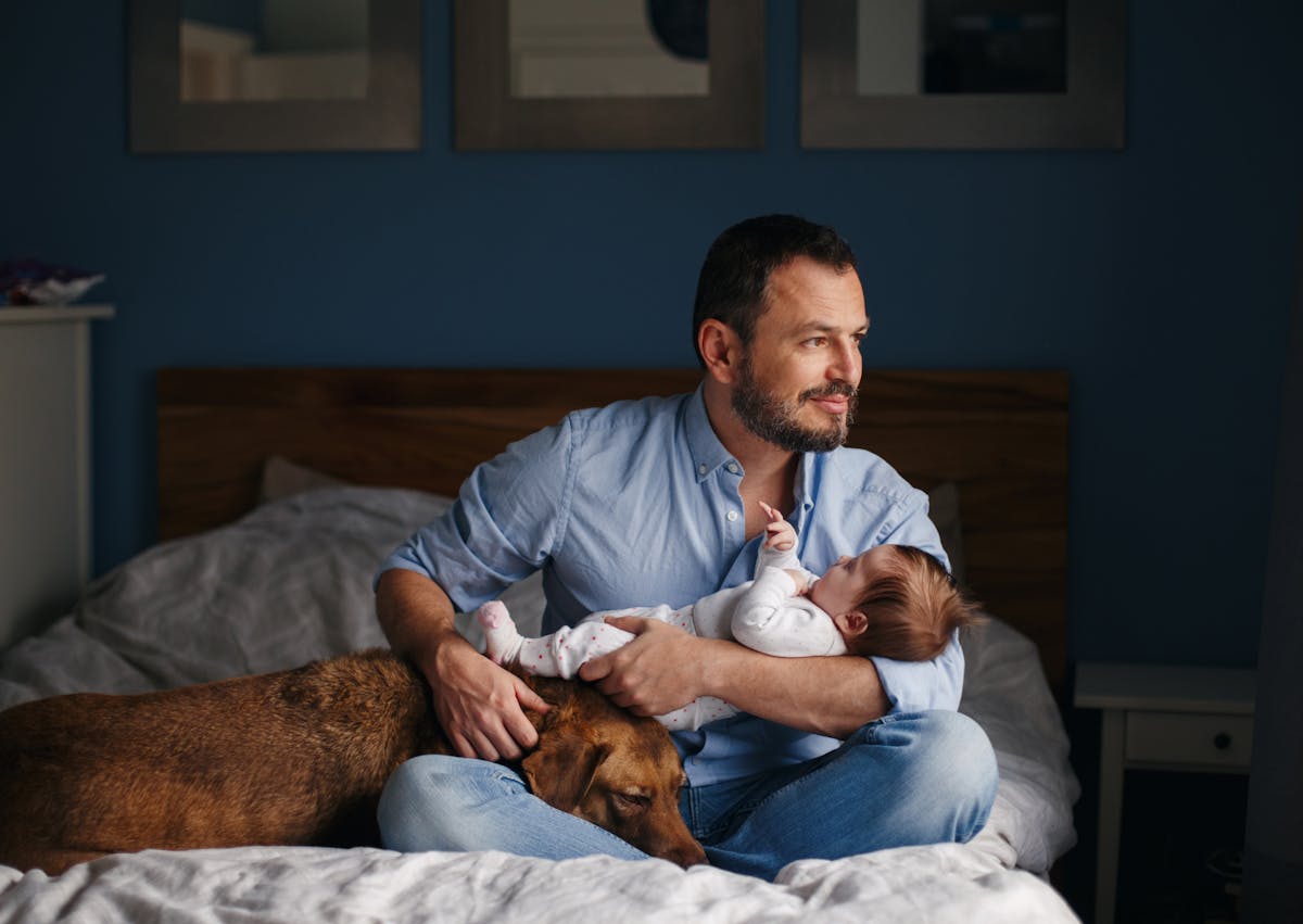 un pèere qui tient son enfant dans les bras, il y a son chien couché près d'eux