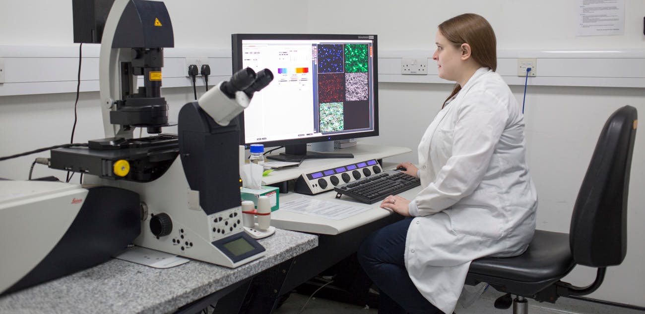 Scientist in a lab with a lab coat, looking at data on the computer.