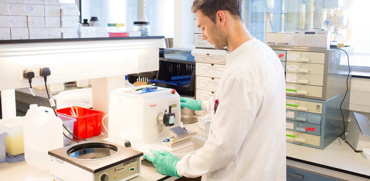 Scientist in a lab with a lab coat, looking at samples.