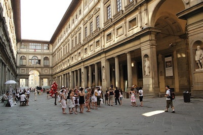 Tourists exploring the grand ground floor of the Uffizi Gallery, with its statues and arches basking in the Florence sunlight