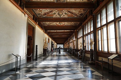 Elegant interior of the Uffizi Gallery's first floor with checkered floors, lined with classical statues and richly decorated ceilings