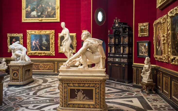 Opulent red room in Uffizi Gallery with Renaissance sculptures and lavish golden framed paintings, intricate marble floor designs enhancing the historical art experience