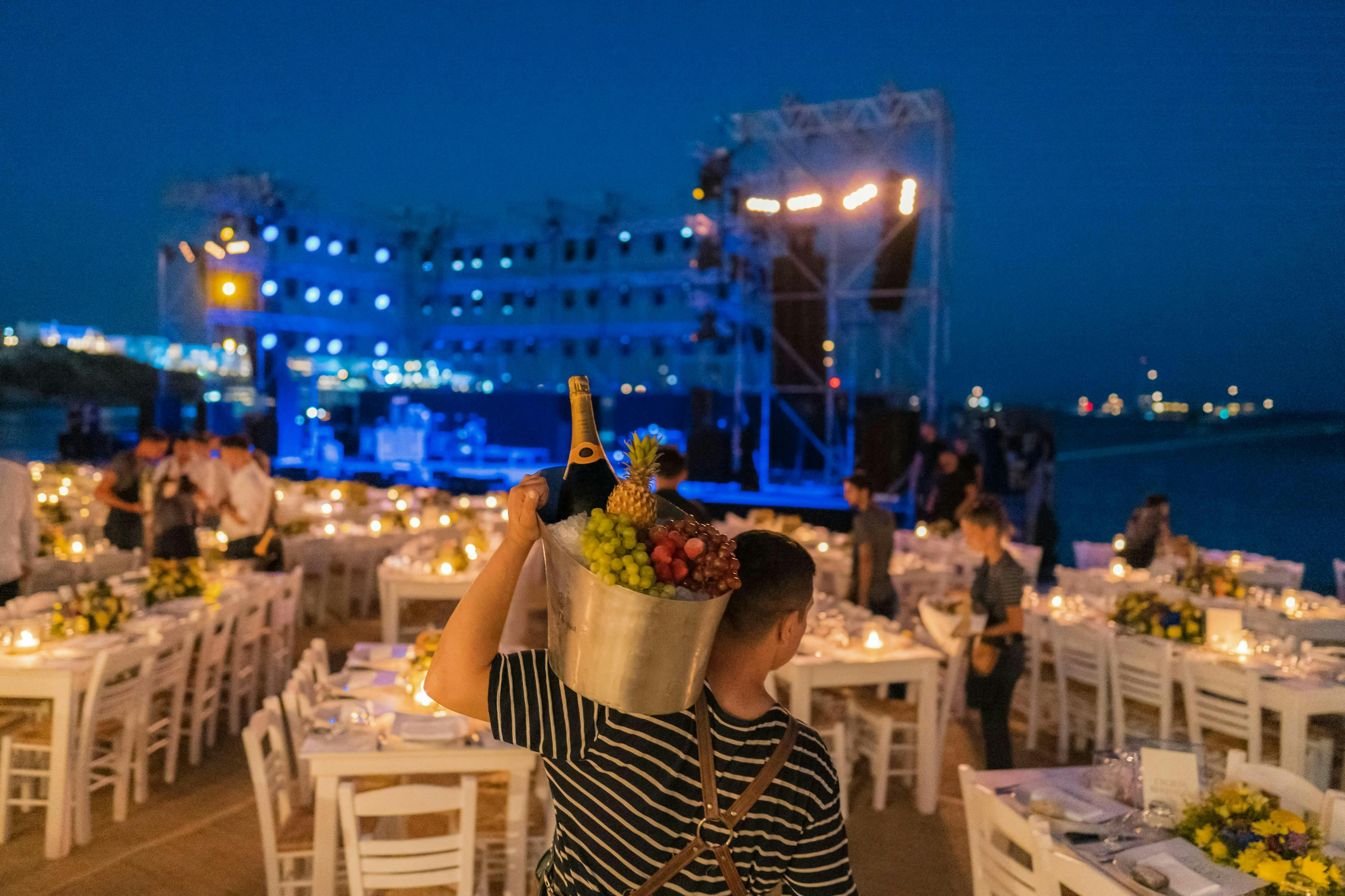 Dinner table set up, man carrying bucket with champagne and stage in background