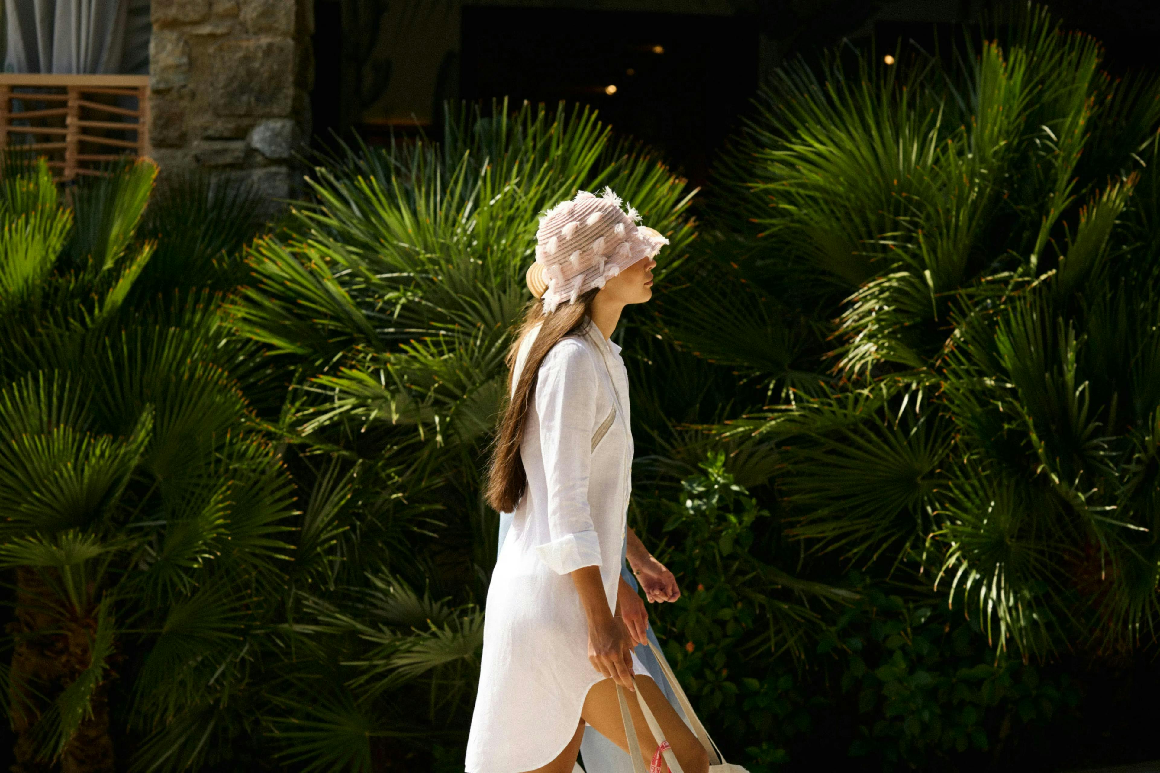 Girl wearing a bucket hat, walking alongside palm trees