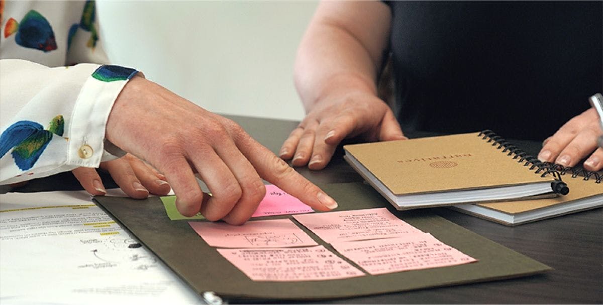 Close up of two people's hands pointing while working together with papers on a table