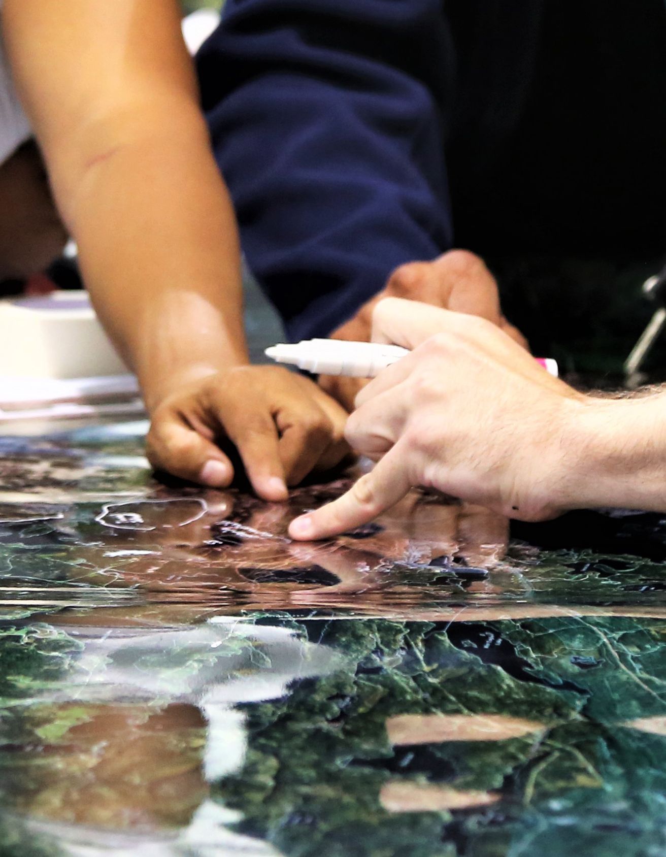 Close up of a mapping session with one hand pointing on the map and another pointing with a marker in hand