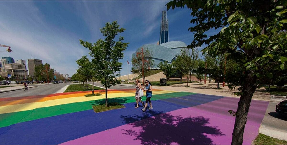Two women walking across a painted rainbow crosswalk