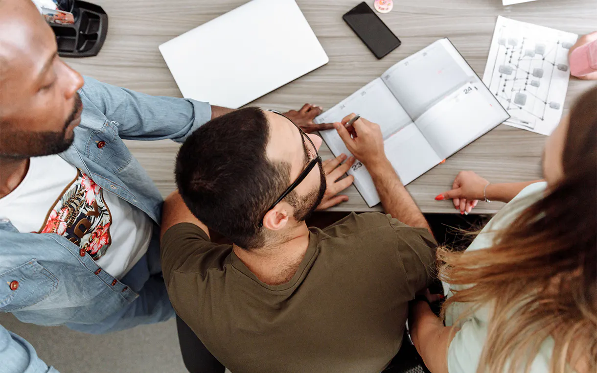 An overhead view of people at a table talking and writing in a notebook