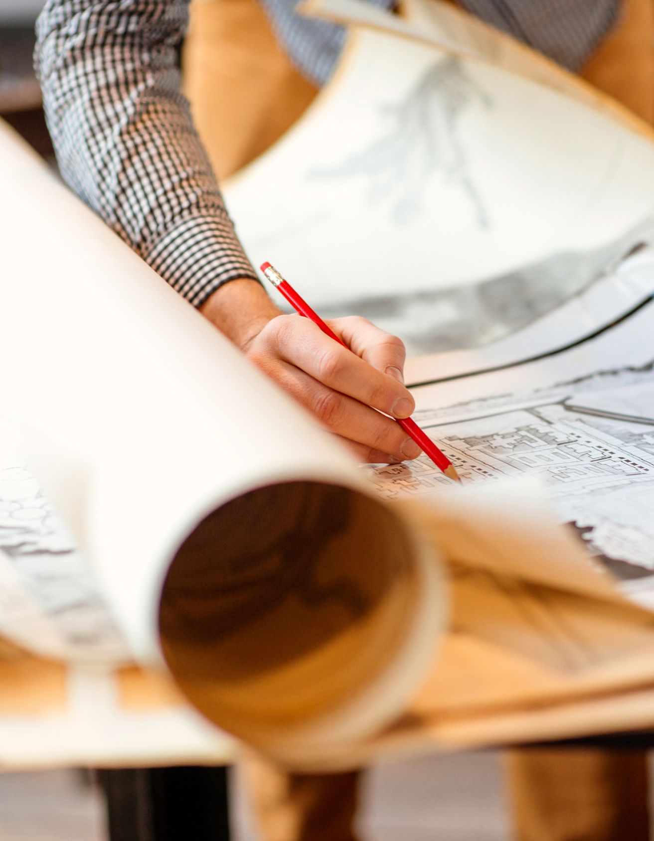 Hand writing with a red pencil on rolled up papers of architectural drawings
