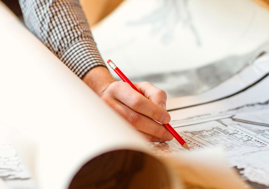 Hand writing with a red pencil on rolled up papers of architectural drawings