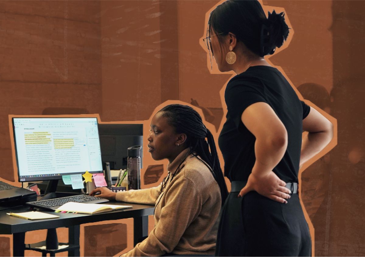 A woman standing and a woman sitting both looking at a computer screen