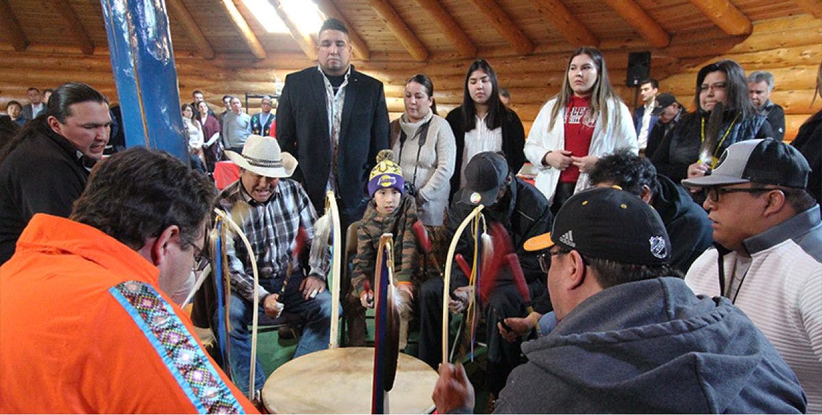 A group of Indigenous people gather around a customary drum