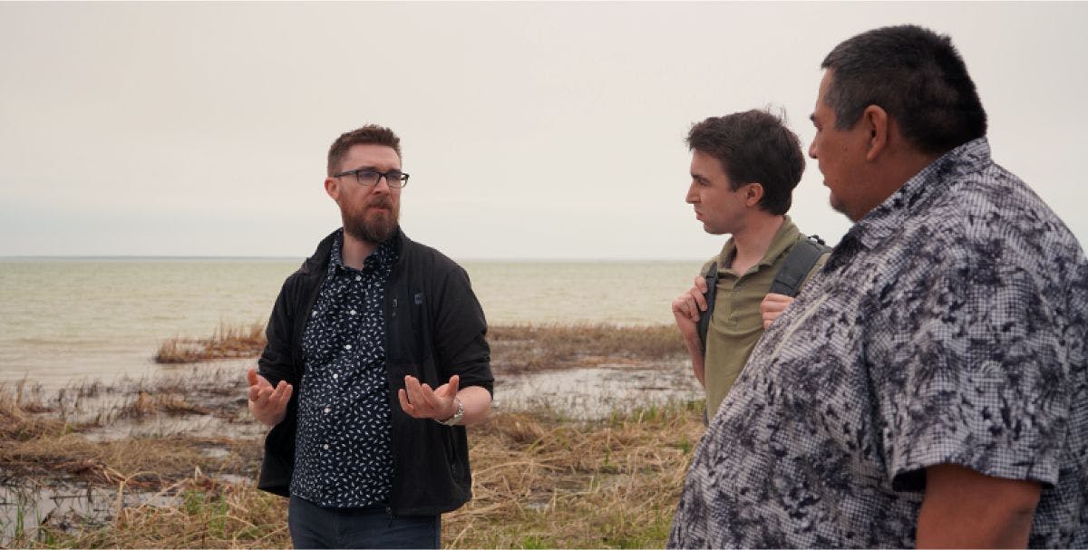 Three men in discussion while walking along the shoreline