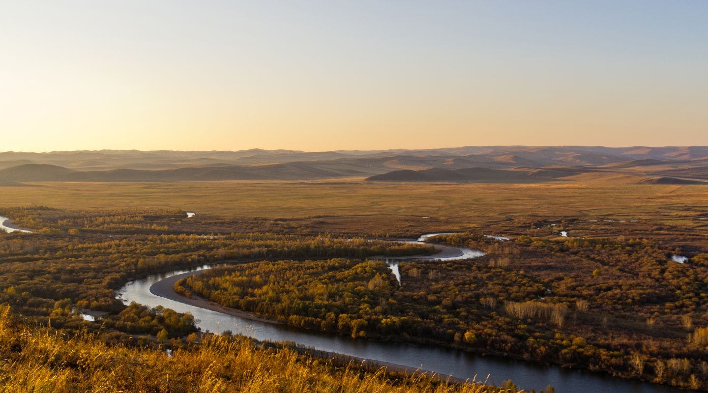 Aerial view of a scenic landscape at sunset with a river flowing through the grass