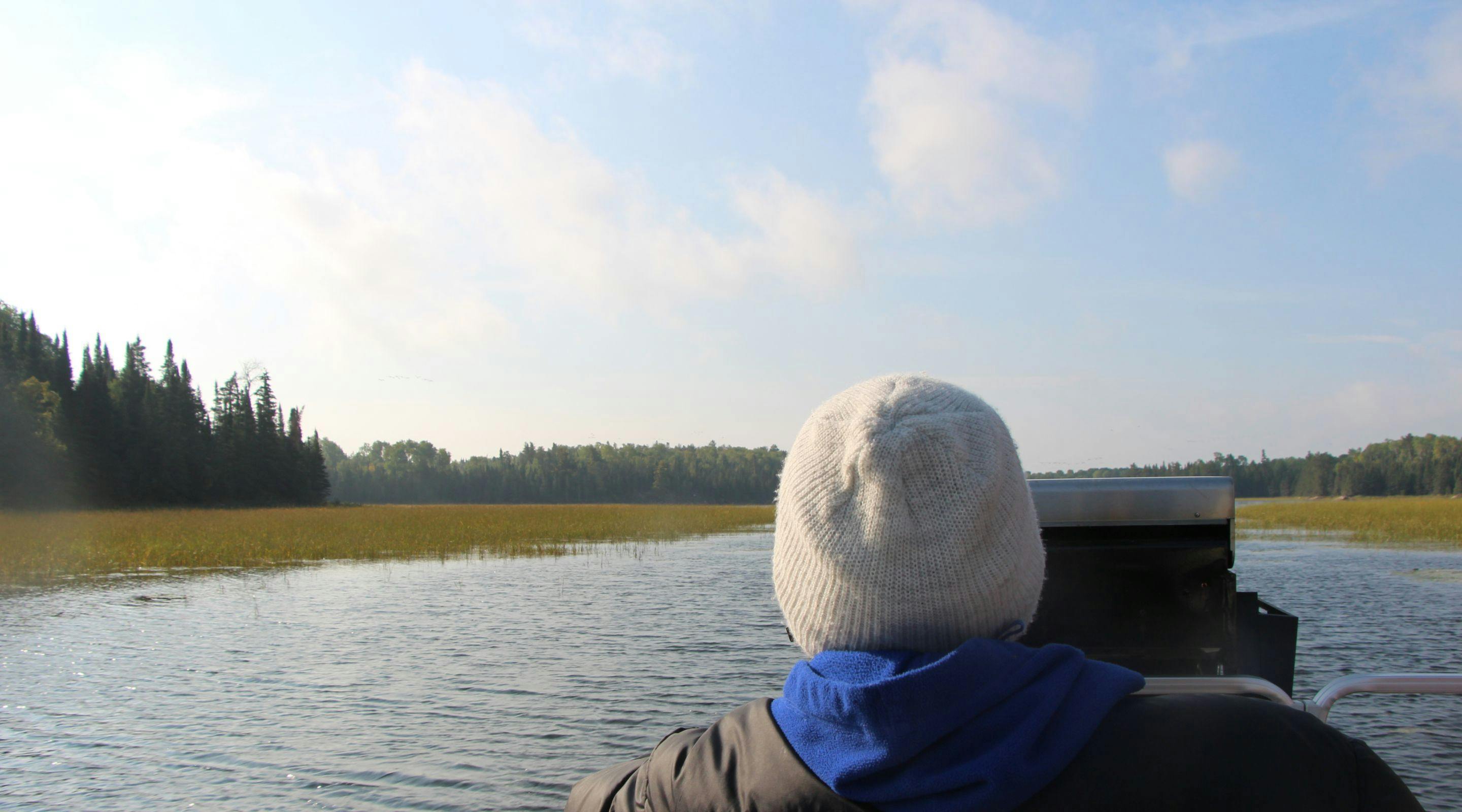 The back of a person wearing a toque jacket sitting in a boat on the river