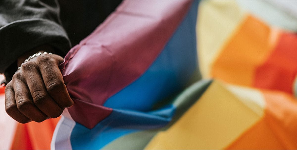 Close up of a hand holding a rainbow flag