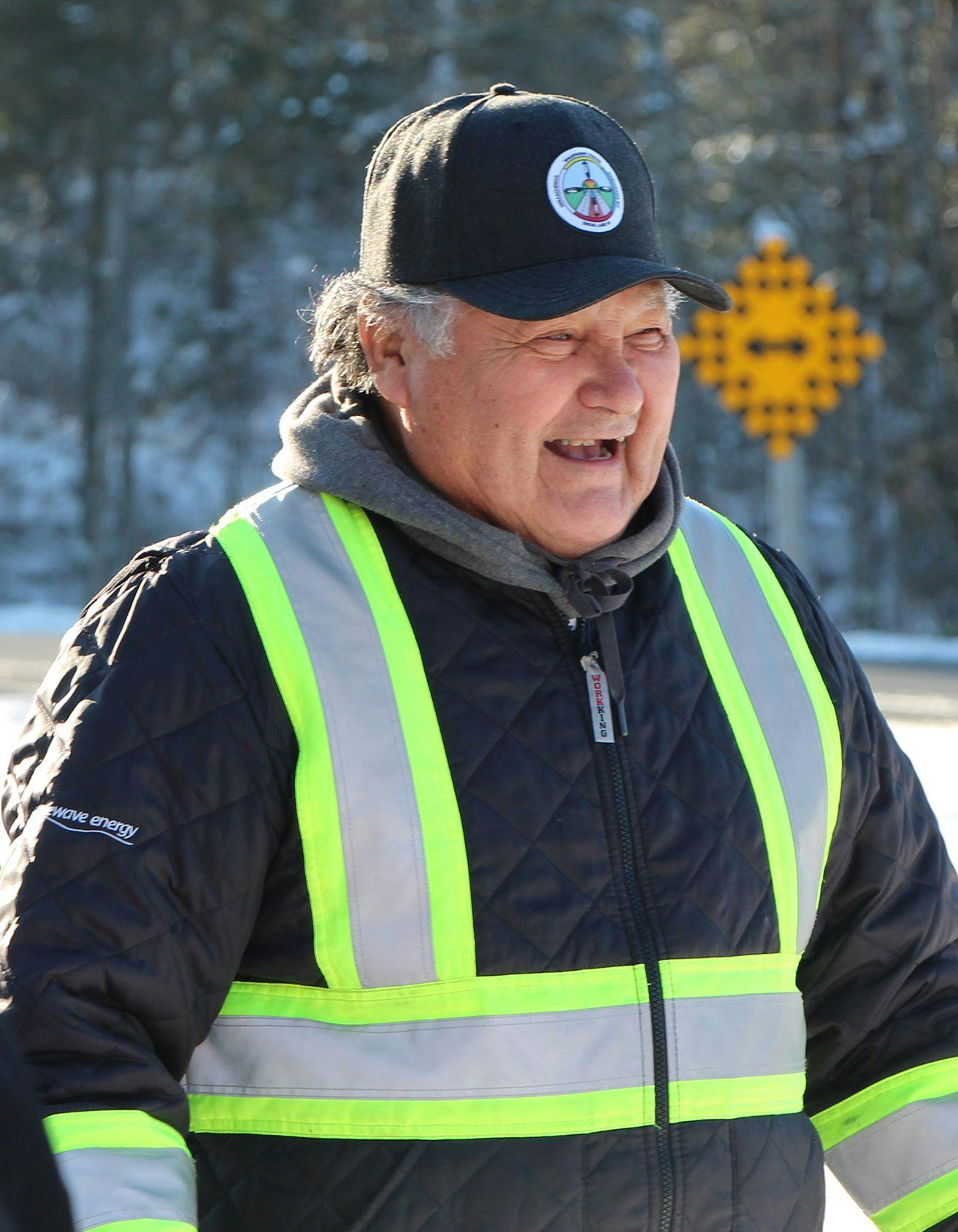 Elderly man smiling while wearing a safety jacket and ball cap