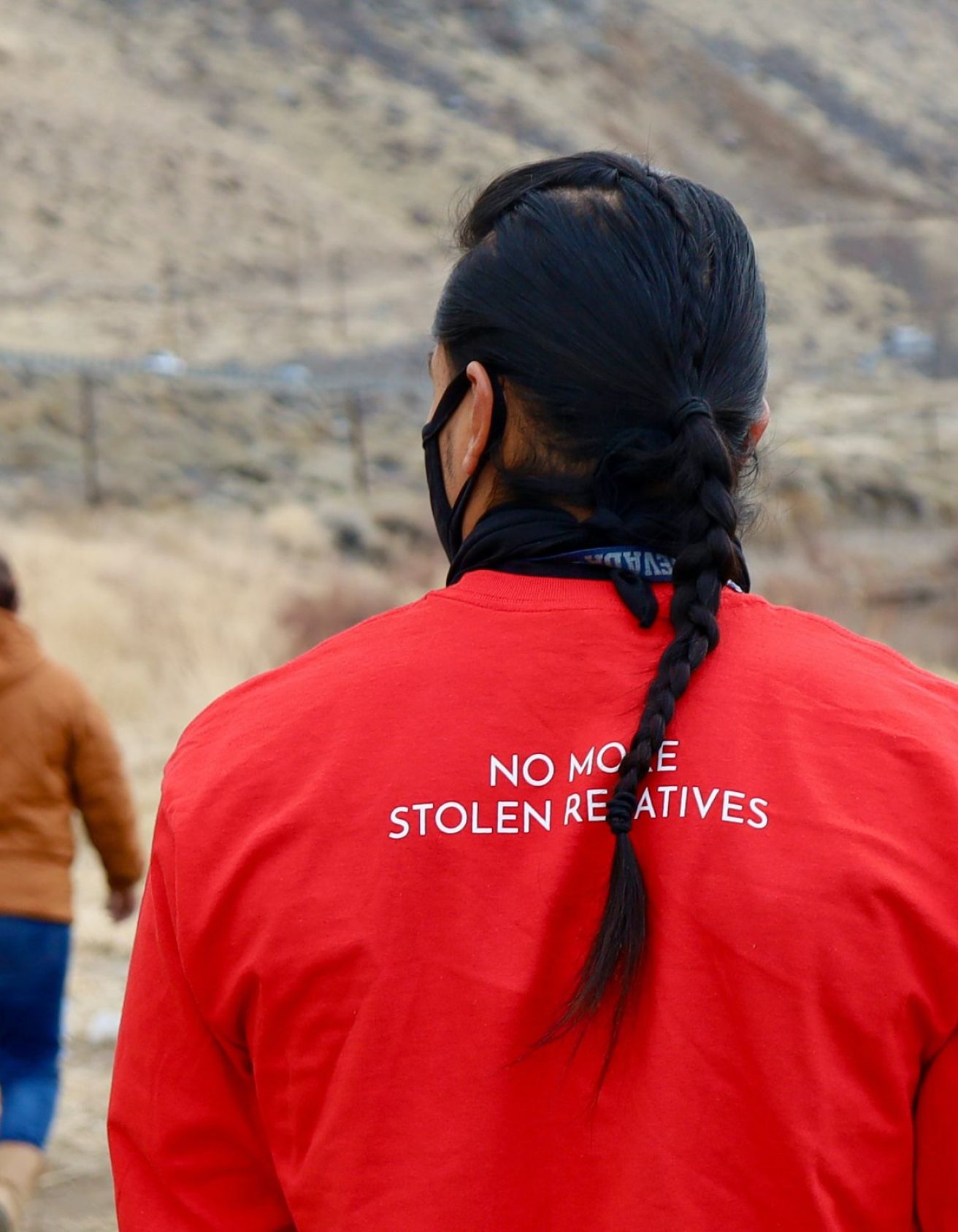 Back of man wearing red shirt that says "No more stolen relatives" while walking outdoors
