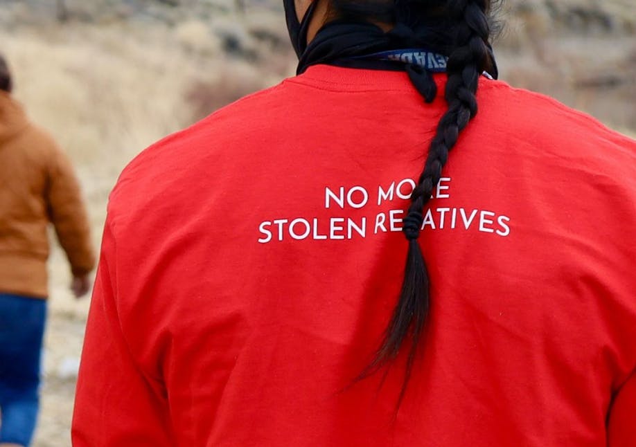 Back of man wearing red shirt that says "No more stolen relatives" while walking outdoors