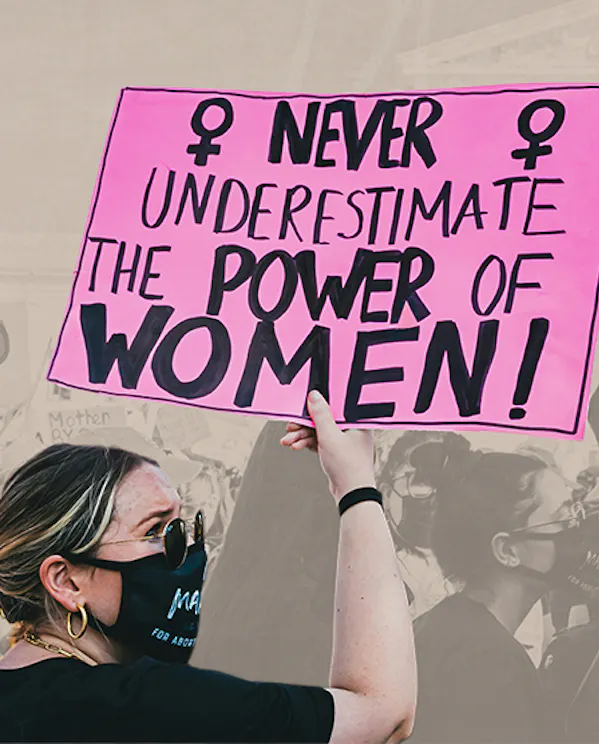 A woman holds a sign at a protest reading 'Never underestimate the power of a women!'