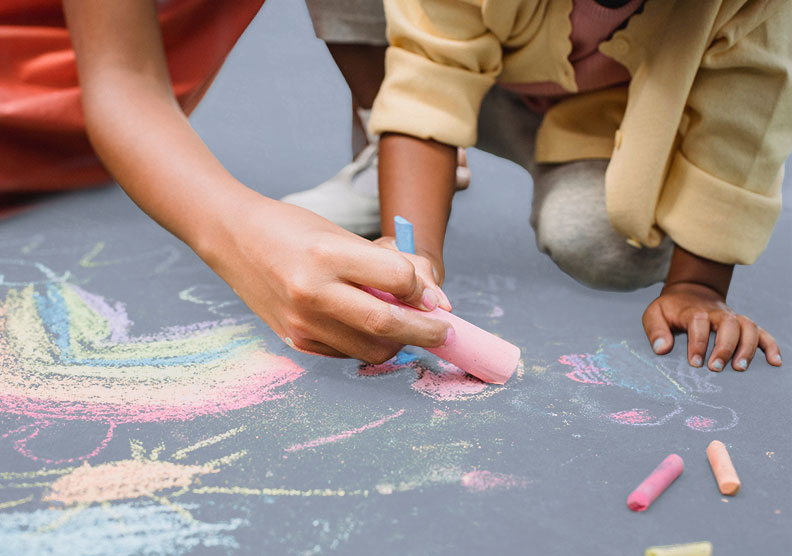 Children drawing on a sidewalk with a variety of coloured chalks