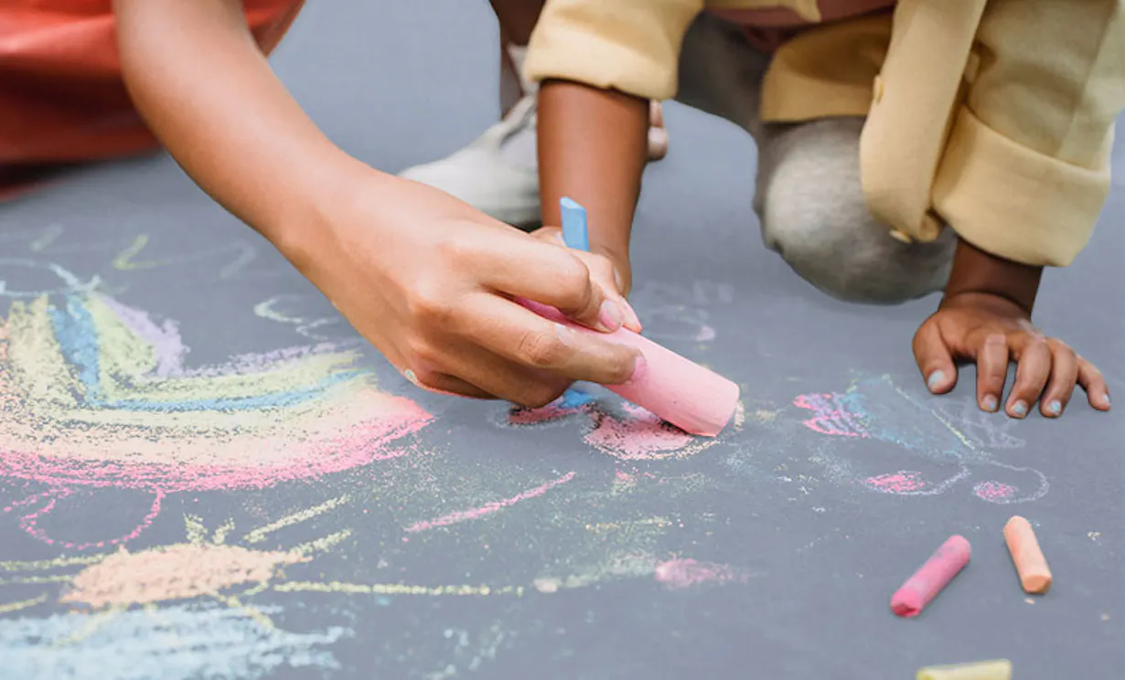 Children drawing on a sidewalk with a variety of coloured chalks