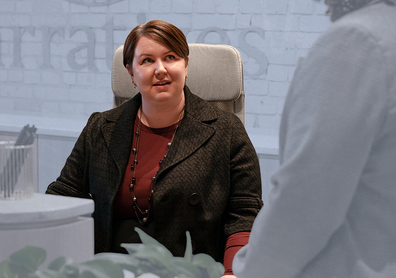 A woman sits at a desk talking to a coworker