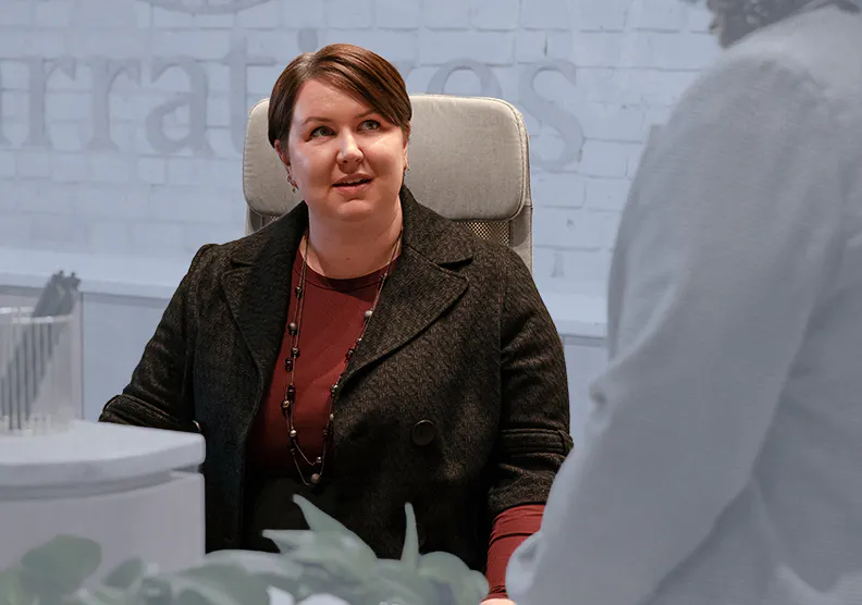 A woman sits at a desk talking to a coworker