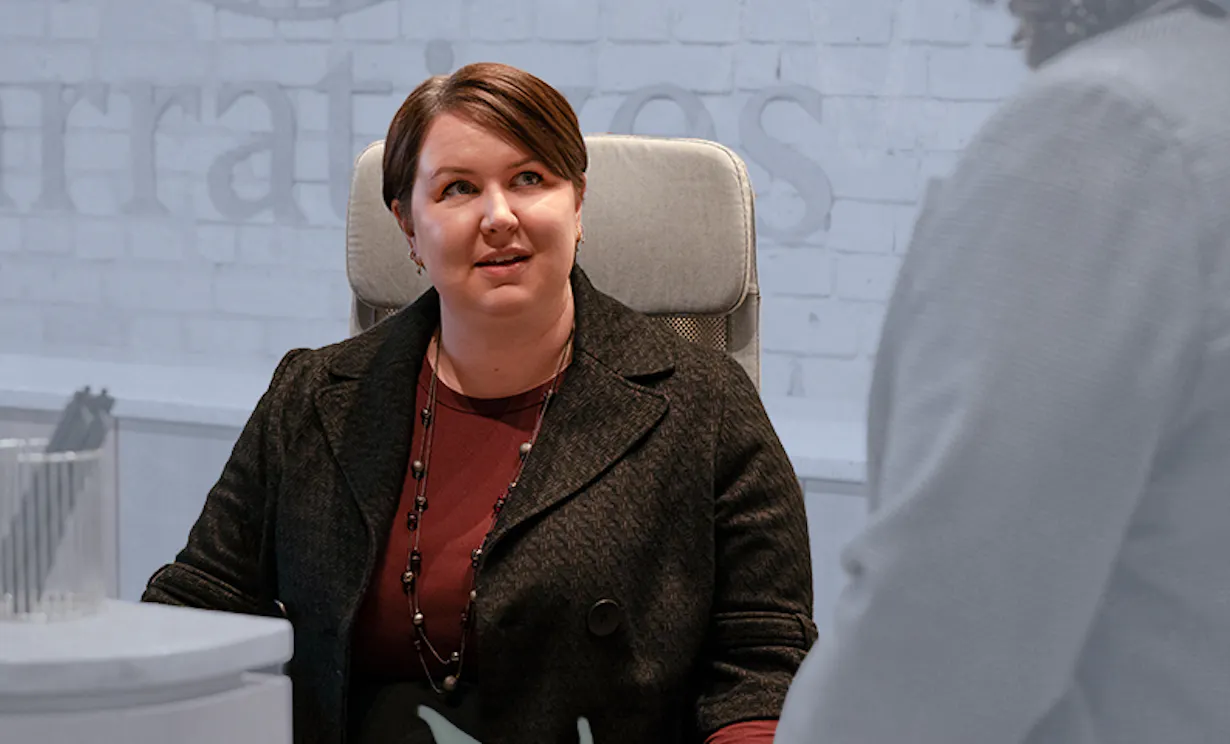 A woman sits at a desk talking to a coworker