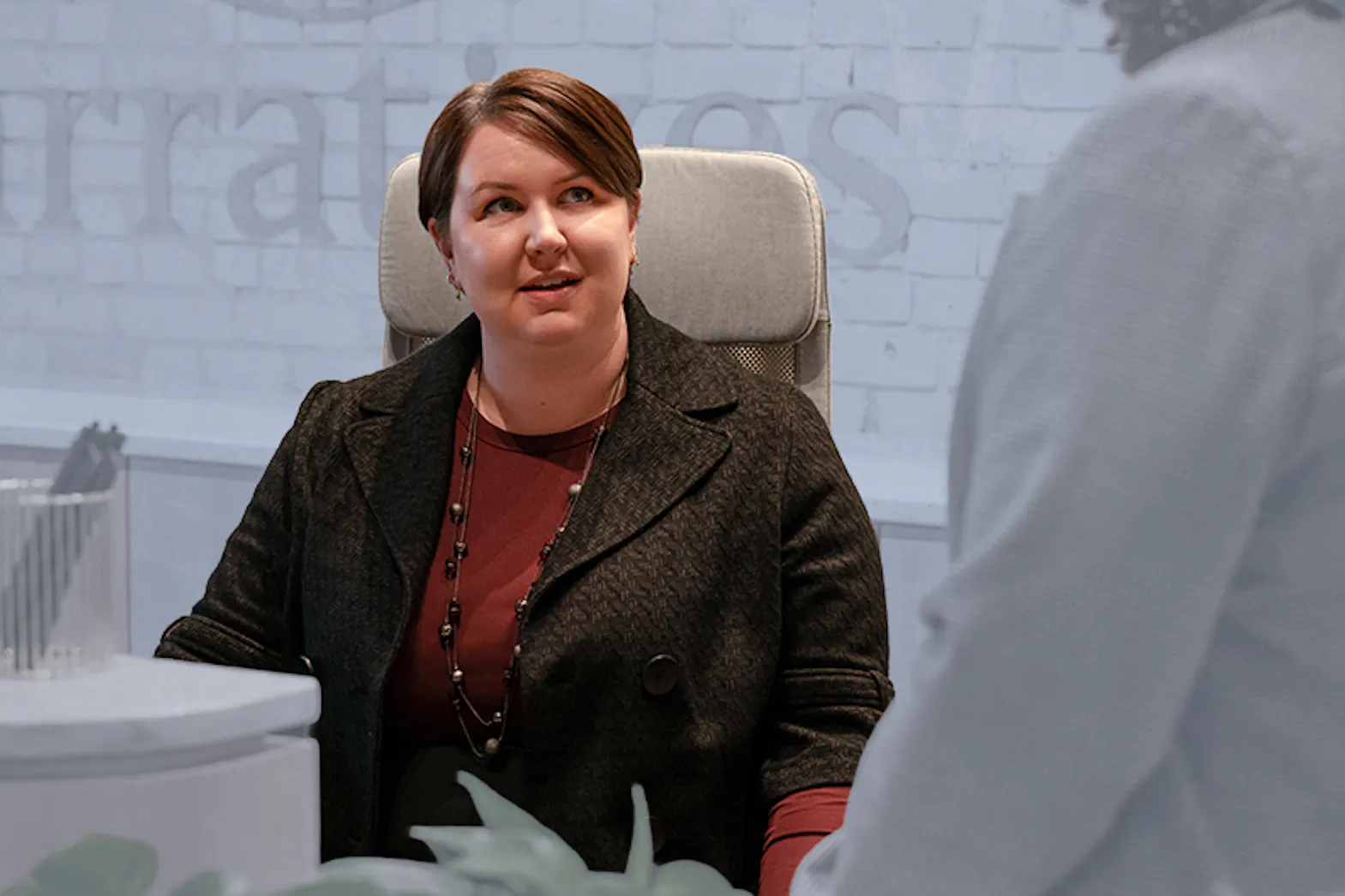 A woman sits at a desk talking to a coworker