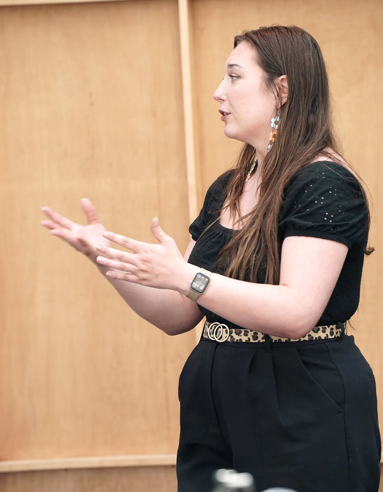 A woman in a black shirt and black pants gestors with her hands over to the left