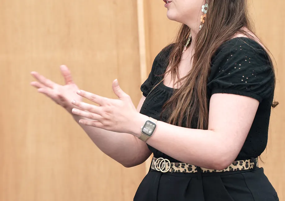 A woman in a black shirt and black pants gestors with her hands over to the left