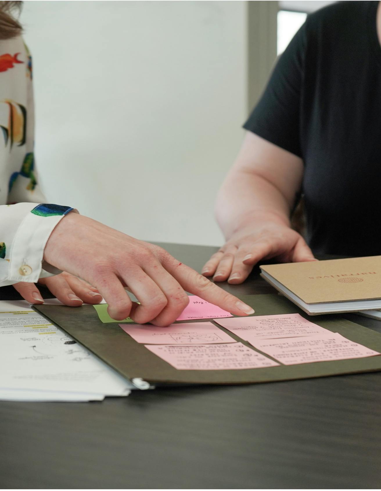 Close up of pink sticky notes being reviewed with one hand pointing to a note