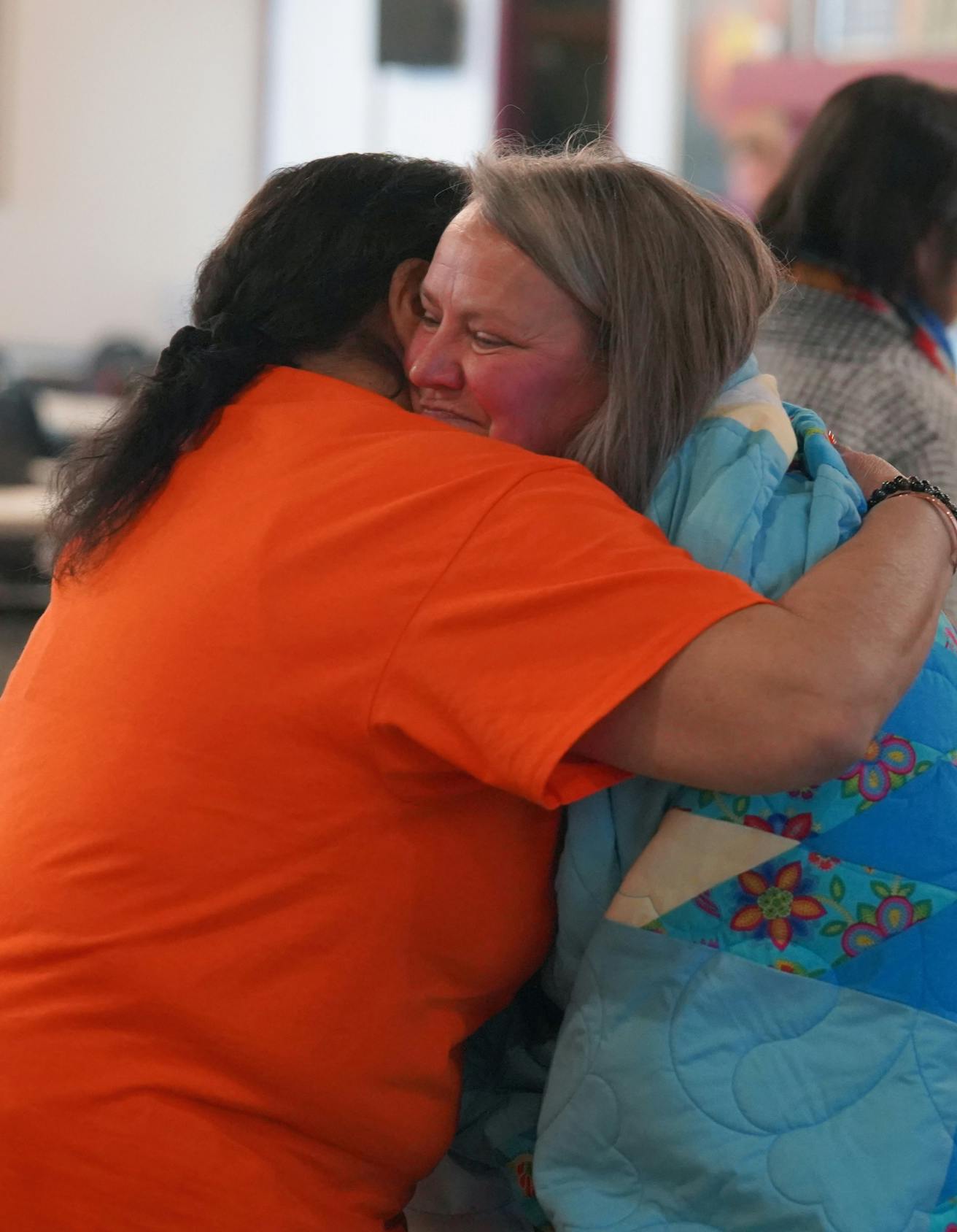 Woman in orange shirt hugging another woman wrapped in a star blanket